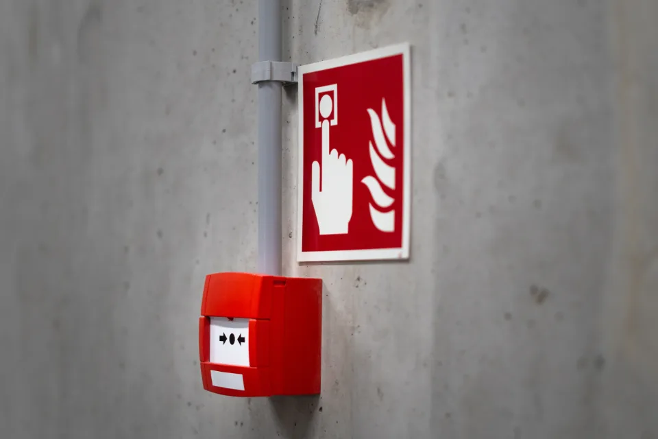 Roter Handfeuermelder mit Brandschutzzeichen an einer Sichtbetonwand in einem Gewerbegebäude
